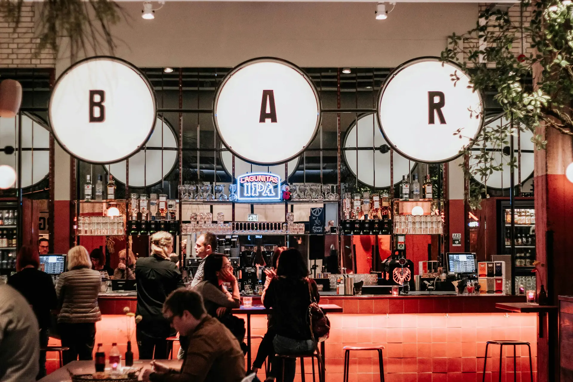 A busy bar with large illuminated BAR signs above the counter
