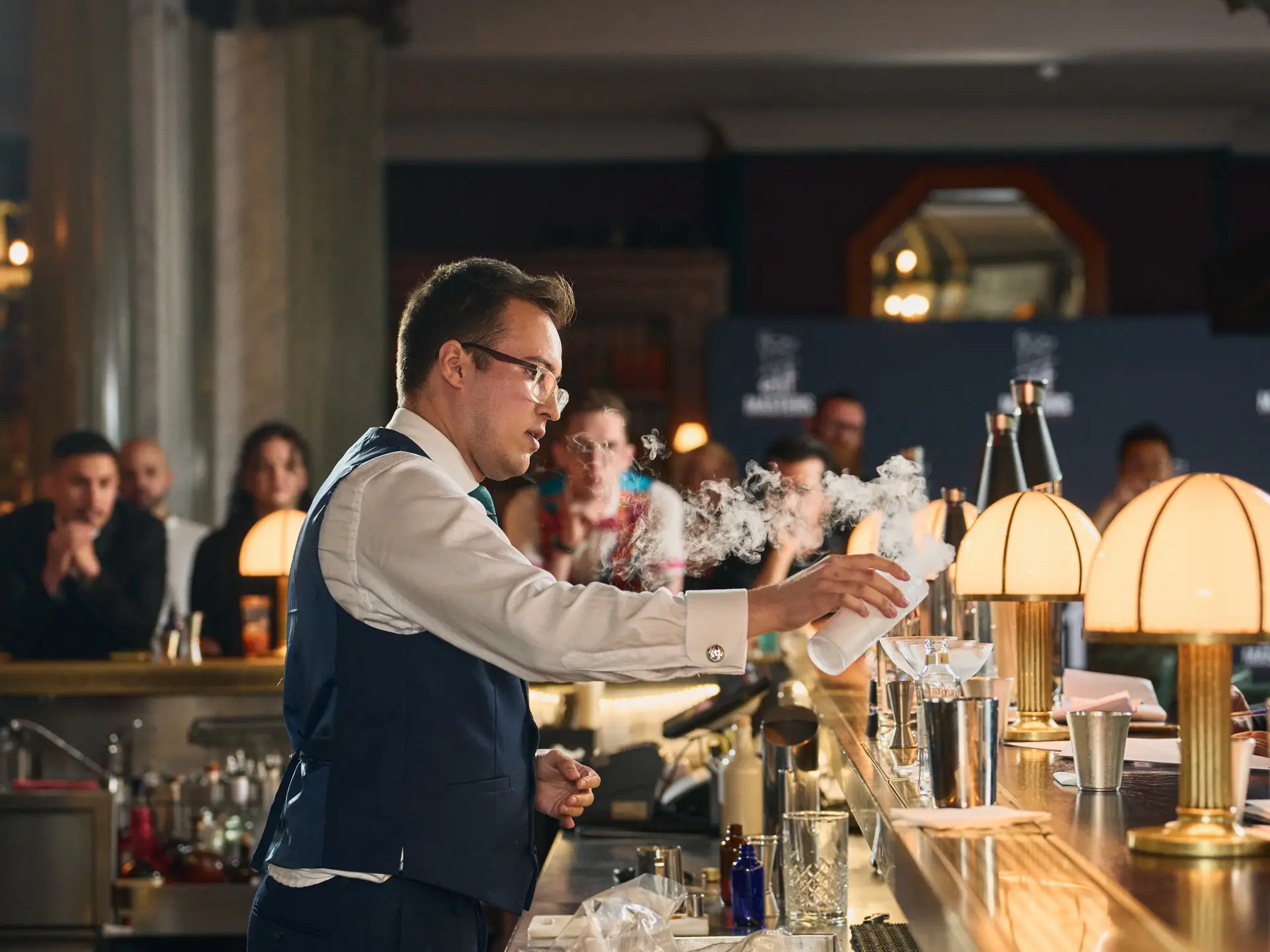 Ein Barkeeper in Weste bereitet vor Gästen in einer belebten Bar einen Drink zu