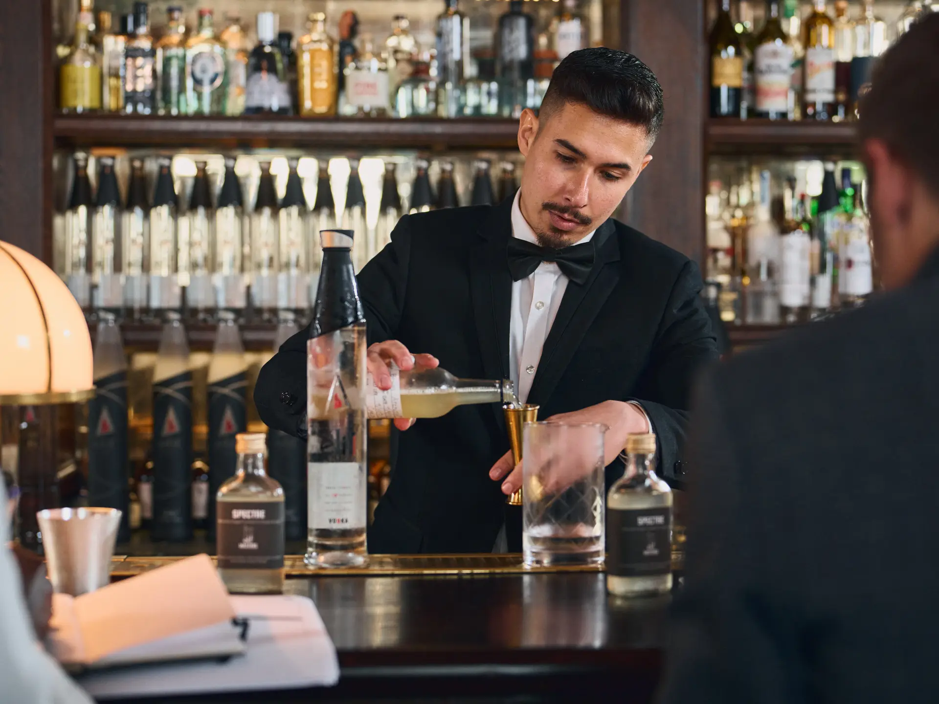 A bartender in a bow tie pouring a drink at the bar
