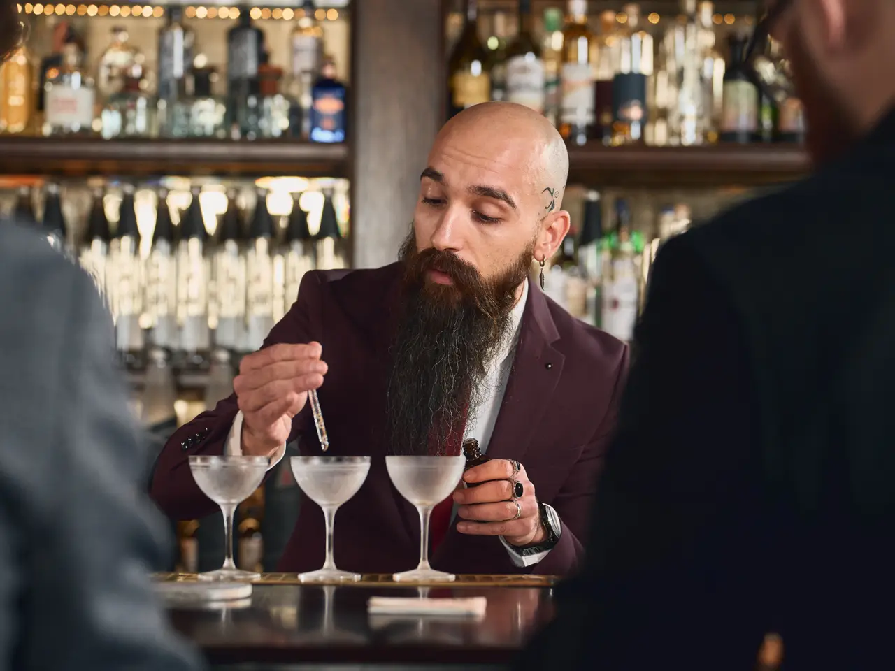 A bearded bartender garnishing two cocktails at the bar