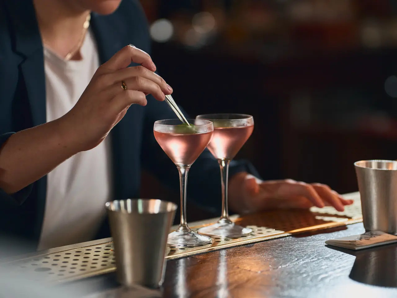 A bartender stirring two pink cocktails