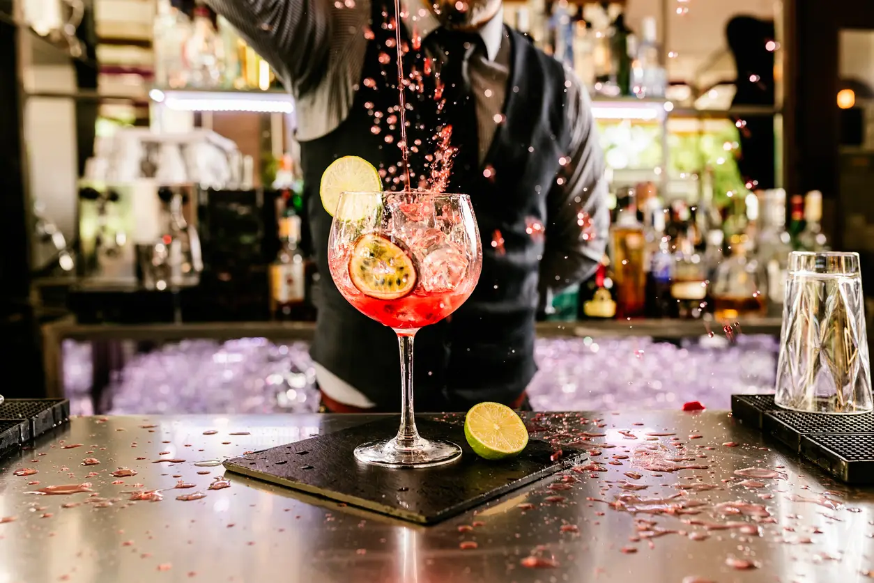 A pink cocktail garnished with lime and grapefruit being splashed into a glass